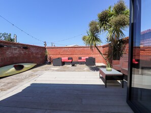 A patio with outdoor furniture, a kayak, and a brick wall. - Ty Haul (Rhosneigr)