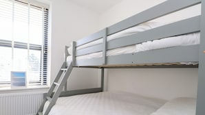 Una cama litera con escalera, ropa de cama blanca, una ventana con persianas y un radiador.
