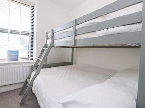 A bunk bed with a ladder, white bedding, a window with blinds, and a radiator. - Ty Haul (Rhosneigr)
