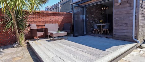 A patio with a wooden deck, a glass door leading to an interior space, and a palm tree.