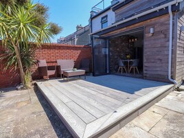Un patio con cubierta de madera, una puerta de vidrio que da a un espacio interior y una palmera.