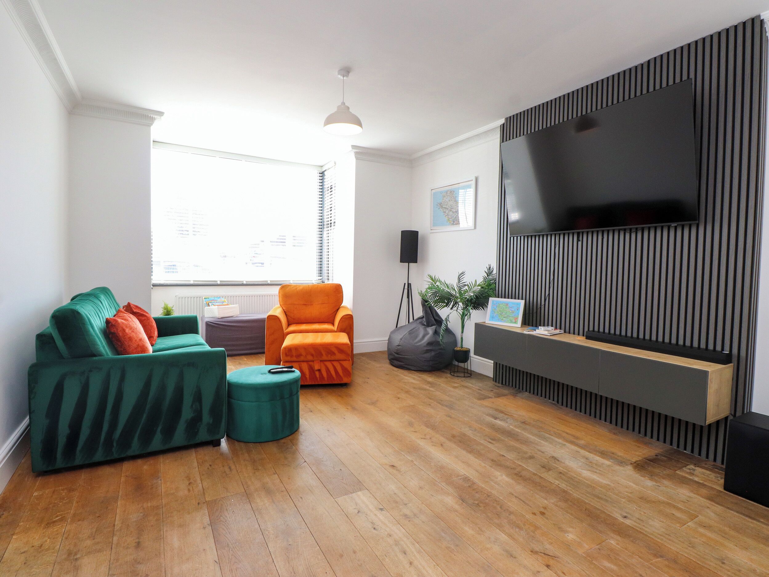 A modern living room with a sofa, ottoman, and armchair, a flat-screen TV, and a potted plant.