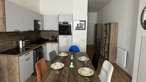 Eine moderne Küche mit integrierten Geräten, eine Essecke mit einem Holztisch für vier Personen und ein großer Spiegel an der Wand.