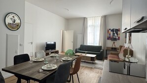 Ein modernes Wohnzimmer mit Essbereich, einer Couch, einem Fernseher und einer Küchenzeile inklusive Kühlschrank.