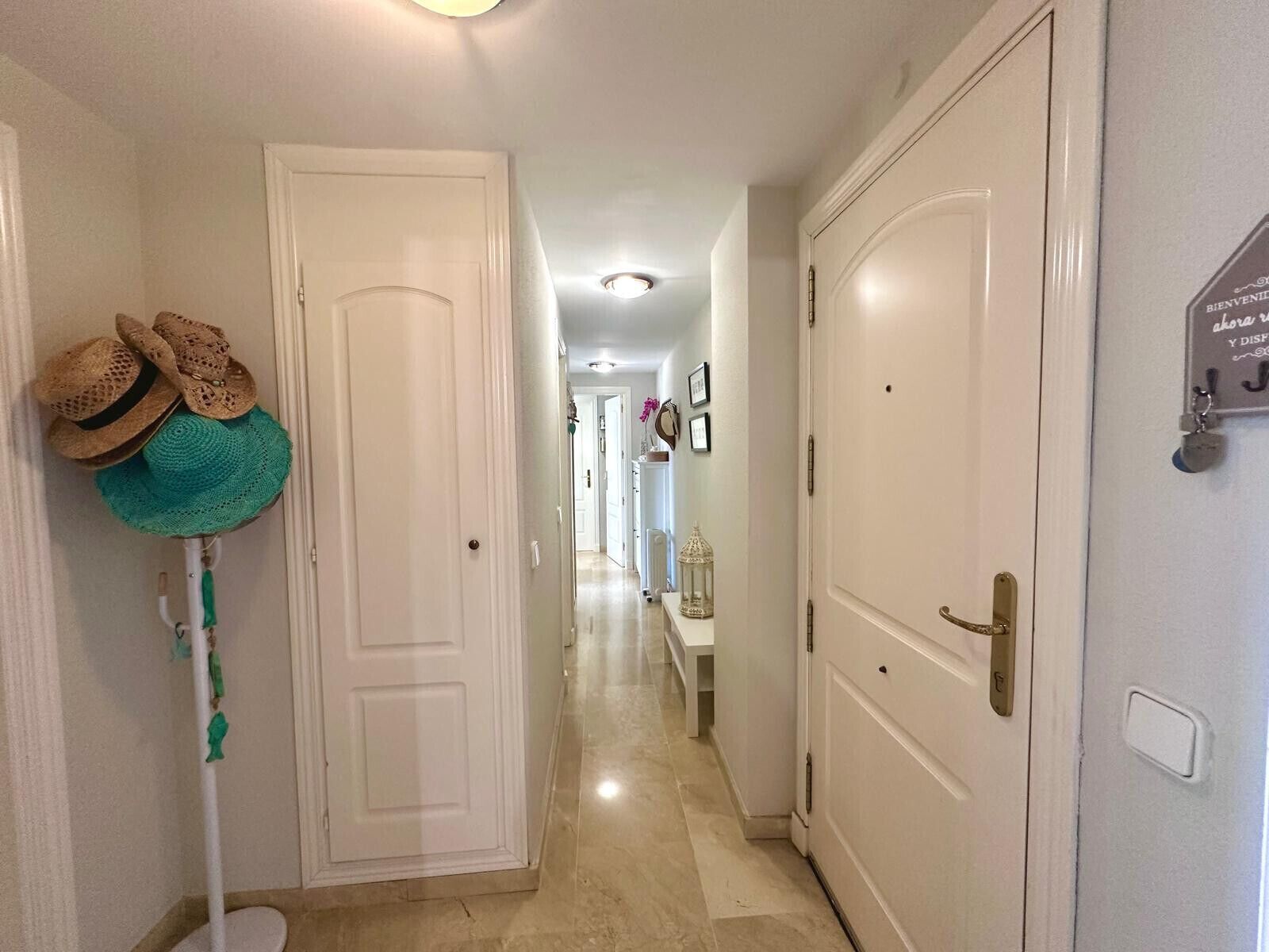 A hallway with white doors, a white wall with a welcome sign, and a green cat tree.