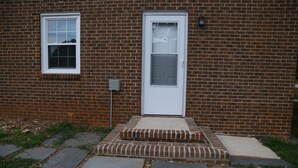 A brick building with a white door, a small window, and a concrete step leading to the entrance.