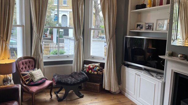 Una habitación con chimenea, televisión, un banco acolchado, una silla y una ventana con cortinas.