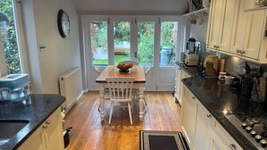 Una cocina con una mesa de madera, armarios blancos y vistas a través de la puerta de cristal.
