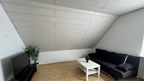 A room with a sloped ceiling, a black sofa, a white coffee table, a TV stand, and a plant. - FeWo Moments - 2 min to E-Park (Rust)