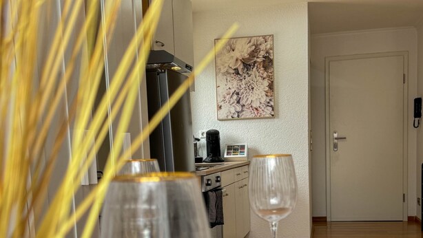 A dining table with plates, a wine glass, and a coffee maker in a modern kitchen with a white door and a floral painting on the wall. - Central Rust Vacation Rental | 5-minute walk to Europapark (Rust)