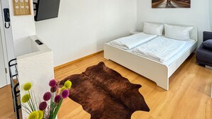 A bedroom with a bed, a TV mounted on the wall, a painting, and a wooden floor. - Central Rust Vacation Rental | 5-minute walk to Europapark (Rust)