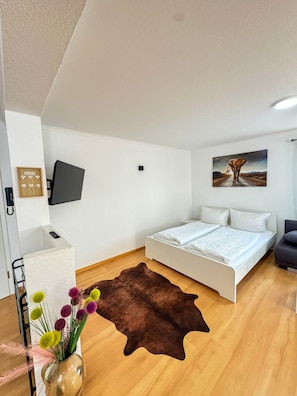 A bedroom with a bed, a TV mounted on the wall, a painting, and a wooden floor. - Central Rust Vacation Rental | 5-minute walk to Europapark (Rust)