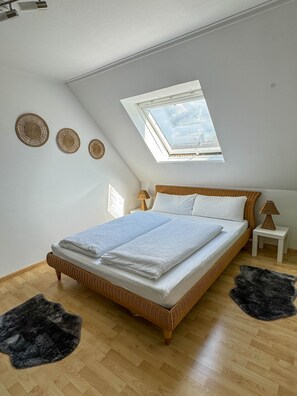 A bedroom with a sloped ceiling, a skylight, a bed with white bedding, two bedside tables, and a small rug. - ONE Vacation Rental - by Europapark (Rust)