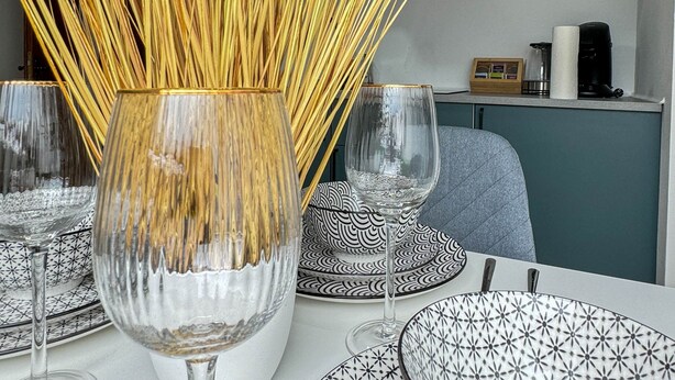 A dining table with a decorative vase of tall, thin, golden reeds, surrounded by patterned plates and wine glasses. - ONE Vacation Rental - by Europapark (Rust)