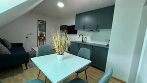 A compact living space with a dining table, two chairs, a kitchenette, a sofa, and a decorative plant. - ONE Vacation Rental - by Europapark (Rust)