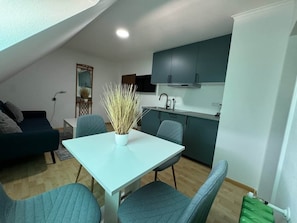 A compact living space with a dining table, two chairs, a kitchenette, a sofa, and a decorative plant. - ONE Vacation Rental - by Europapark (Rust)