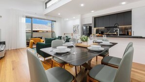 Een moderne eethoek met een tafel voor vier personen, een keuken op de achtergrond en uitzicht buiten.