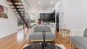 Een moderne woonkamer met een hondentandsofa, een ronde gouden tafel en een trap met houten treden.