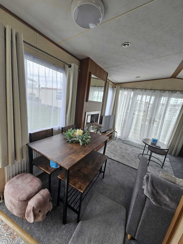 Un espacio habitable compacto con una mesa de comedor, bancos, un sofá y una mesita con un mando a distancia.