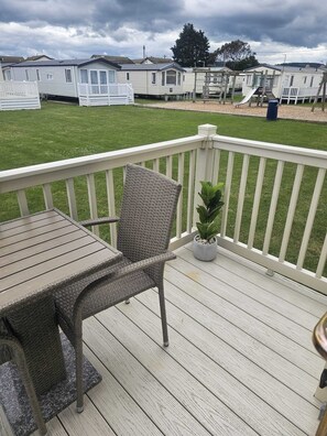Een terras met een tafel, een stoel, een plant in pot en een uitzicht op stacaravans op de achtergrond.