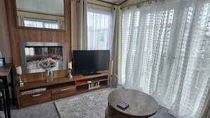Een woonkamer met een televisie, een houten tv-meubel, een tafel en een grote spiegel.