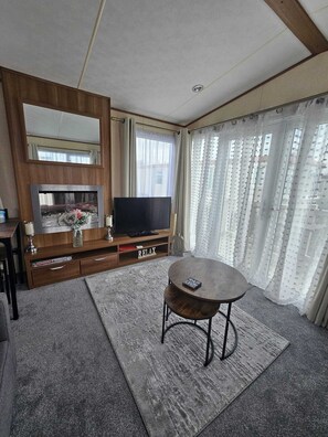 Una sala de estar con televisor, mueble bajo de madera, una mesa y un espejo grande.