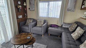 Een woonkamer met een zithoek, een salontafel, een wandklok en een raam met gordijnen.