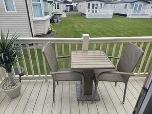 Een balkon met een tafel en stoelen, een bloempot en uitzicht op een grasveld met stacaravans.