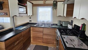 Een kleine keuken met houten kastjes, een magnetron, een spoelbak en een kookplaat.