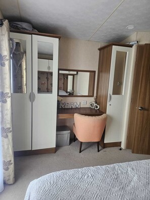 Een slaapkamer met een bed, een bureau, een stoel, een kledingkast en een spiegel.