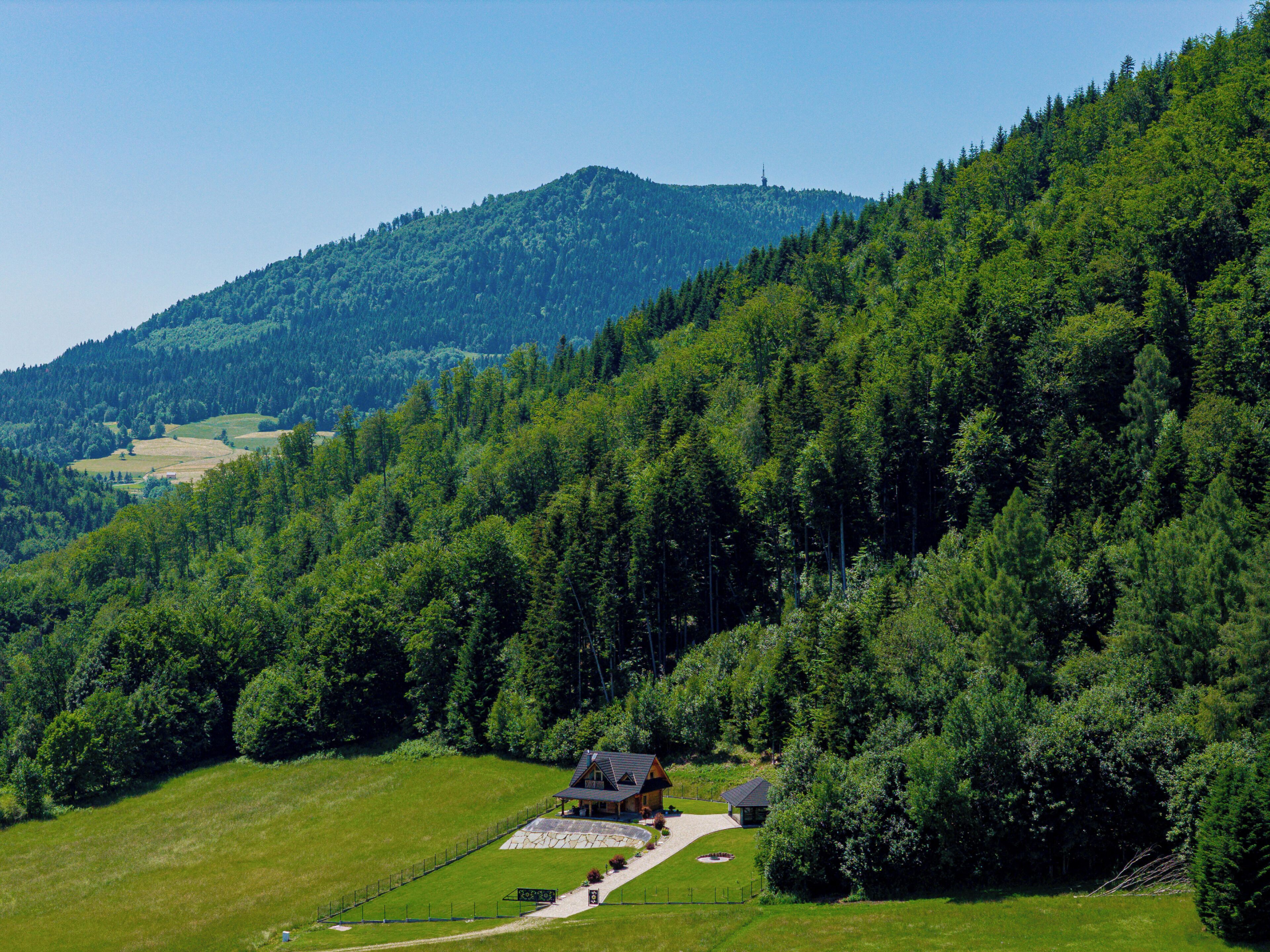 Een landhuis met een stenen terras, omringd door weelderige groene velden en dicht bos.