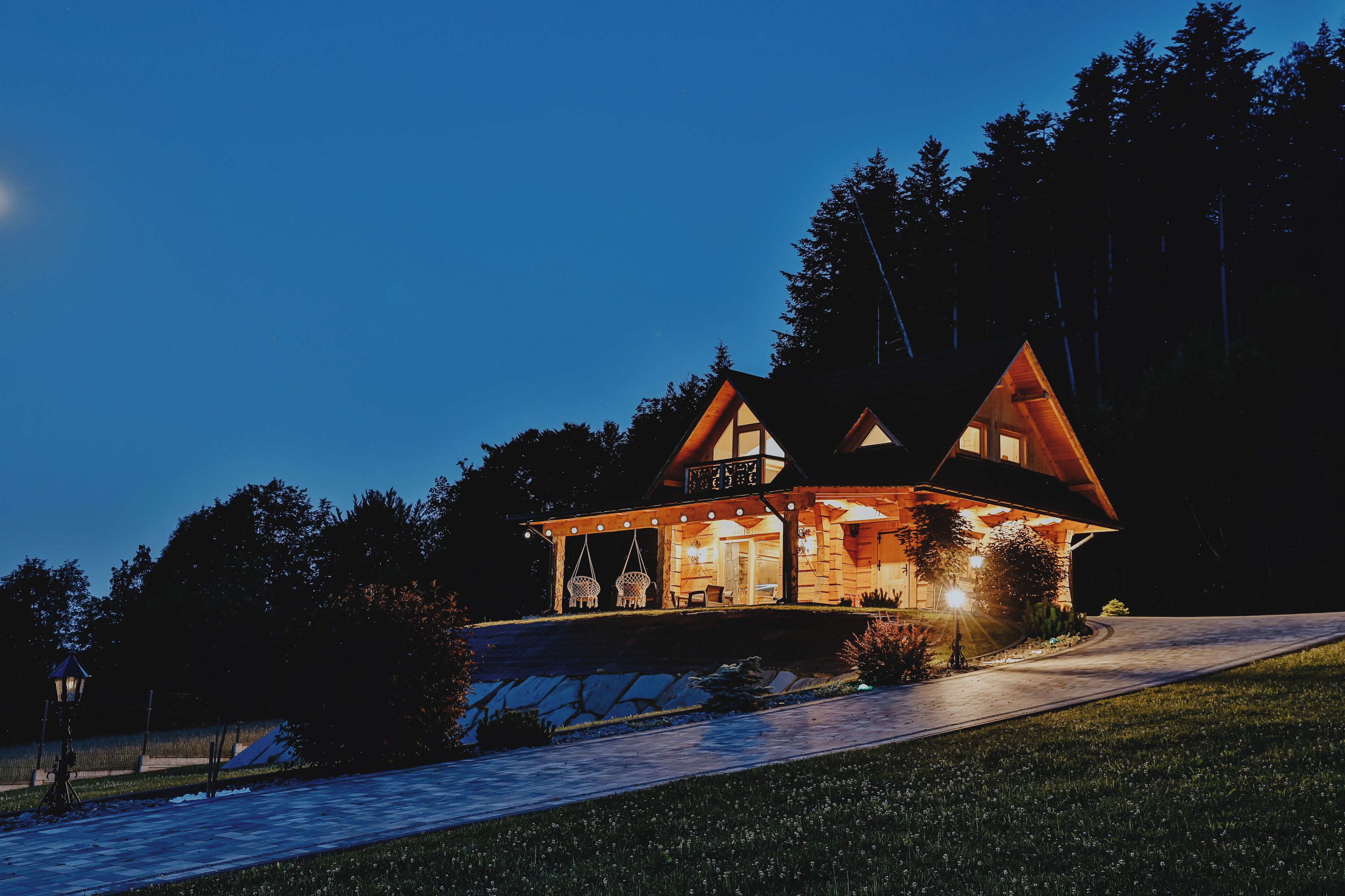 Uma cabana de toras com varanda, lareira e exterior bem iluminado ao entardecer.