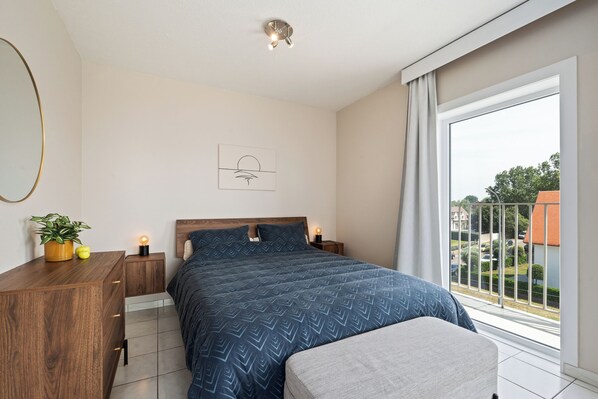 Un dormitorio con una cama grande, mesitas de noche, una planta en maceta y una ventana con vistas al exterior.
