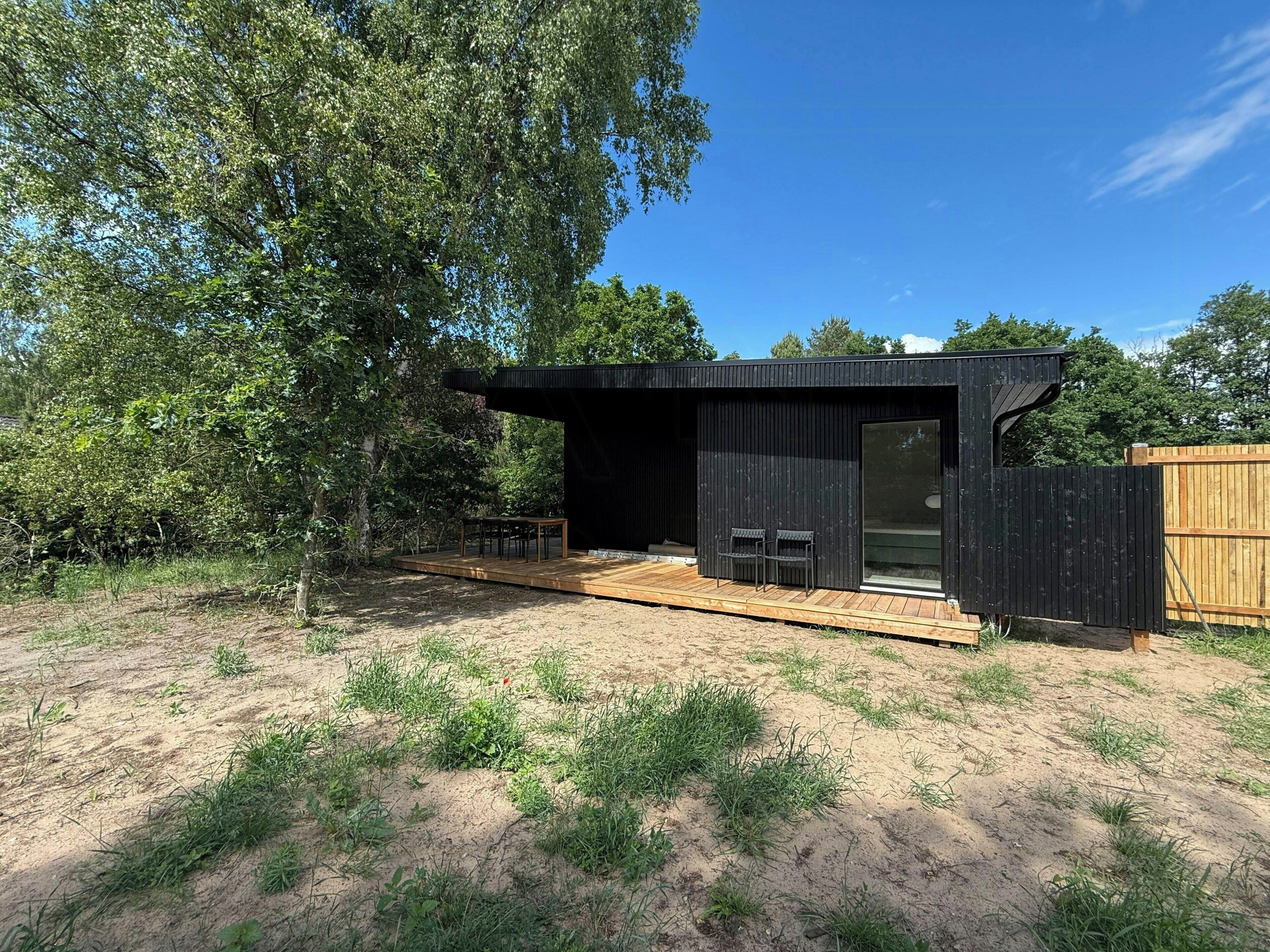 Een moderne buitenconstructie met terras, zitplaatsen en een groot raam.