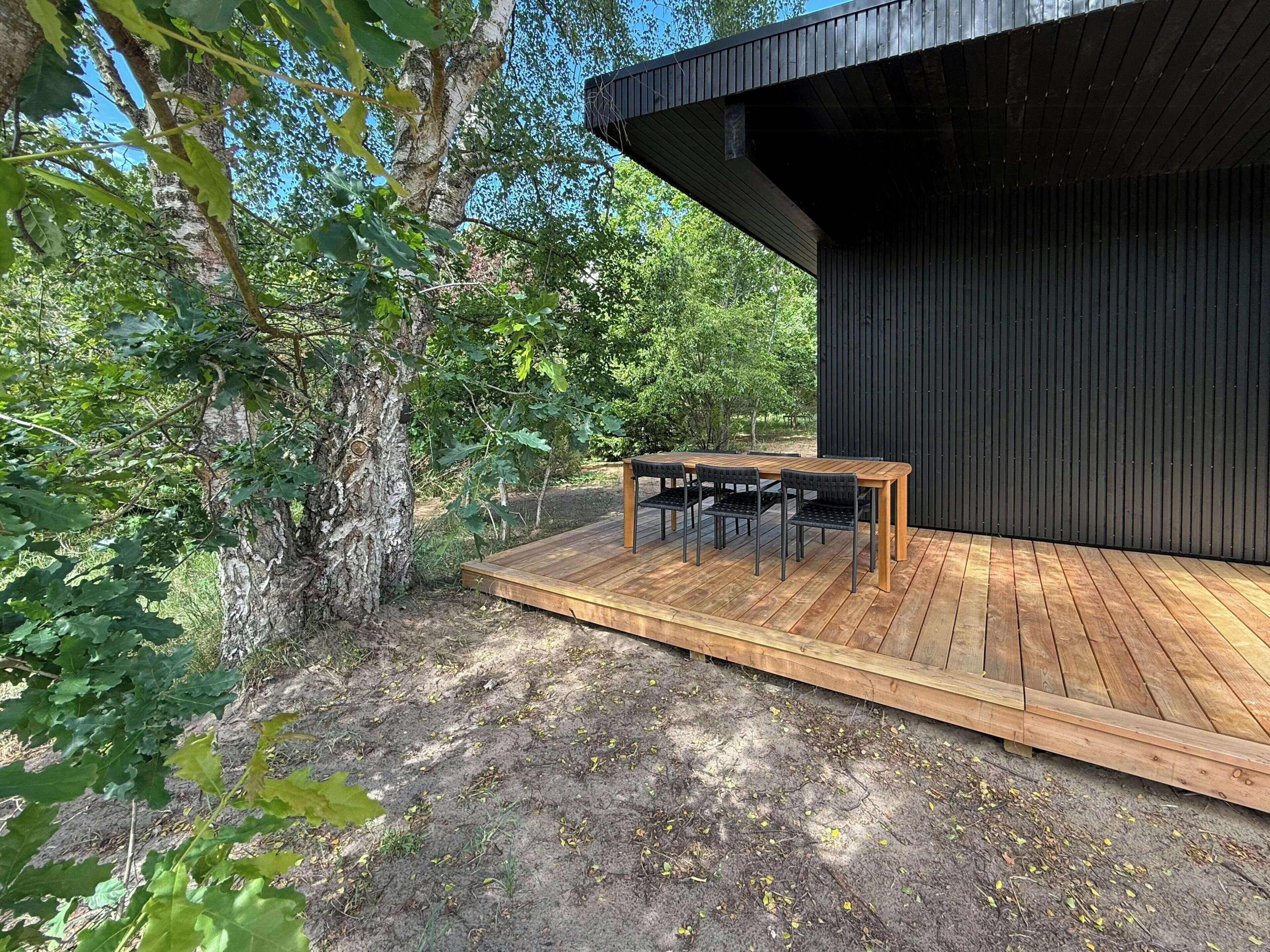 A wooden deck with a table and chairs, surrounded by trees.