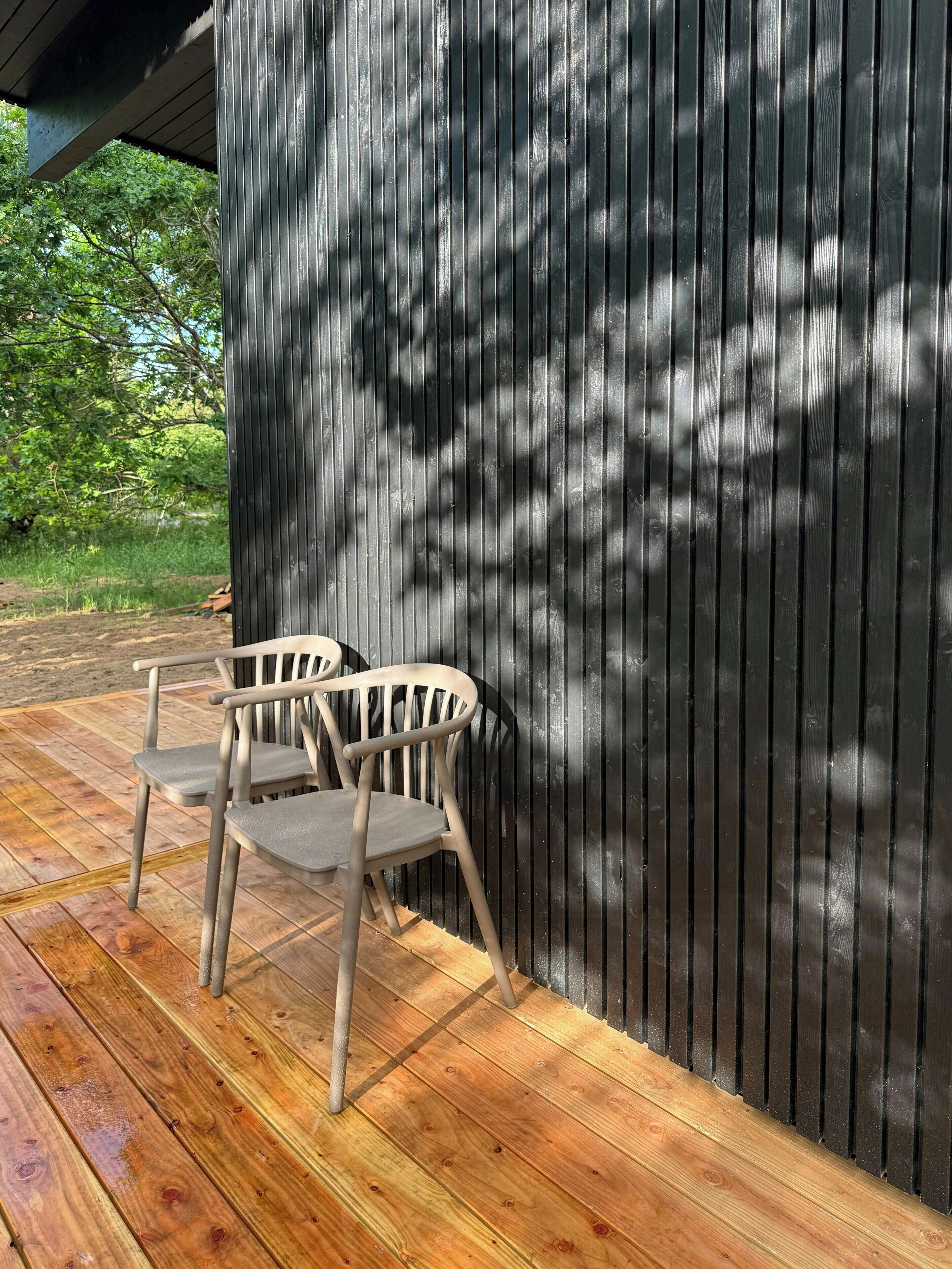 A wooden deck with two chairs and a metal wall.