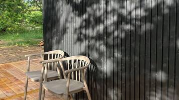 A wooden deck with two chairs and a metal wall.