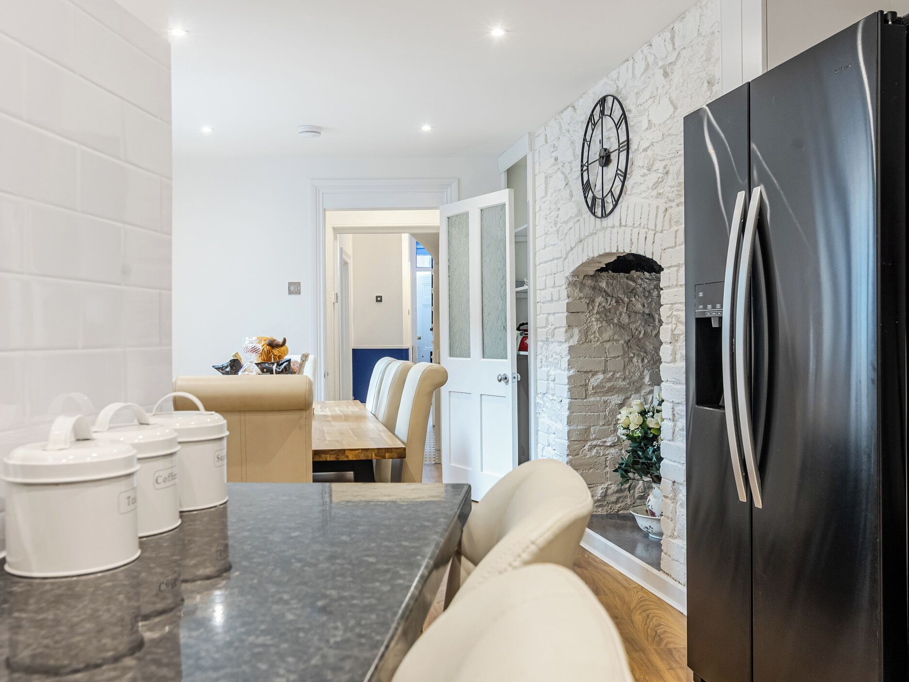A modern kitchen with a stone wall, a black refrigerator, and a dining area with a bench and chairs.