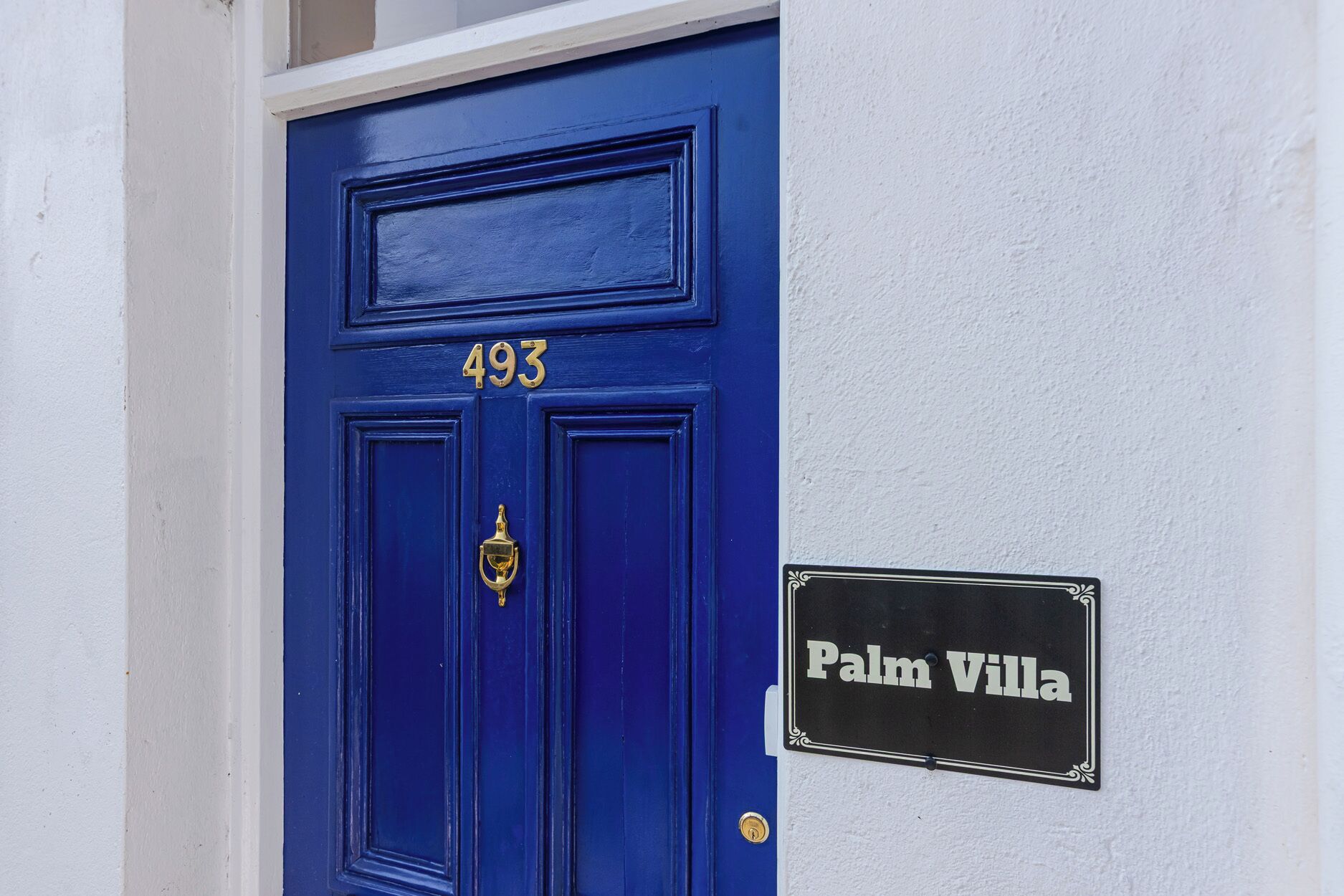A blue door with the number 493 and a sign reading 'Palm Villa'.