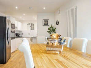 Eine moderne Küche mit weißen Schränken, einem schwarzen Kühlschrank und einem Essbereich mit Holztisch und weißen Stühlen.