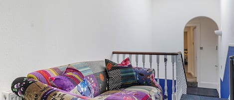 A white-walled room with a colorful sofa, a wooden staircase, and a blue patterned floor.