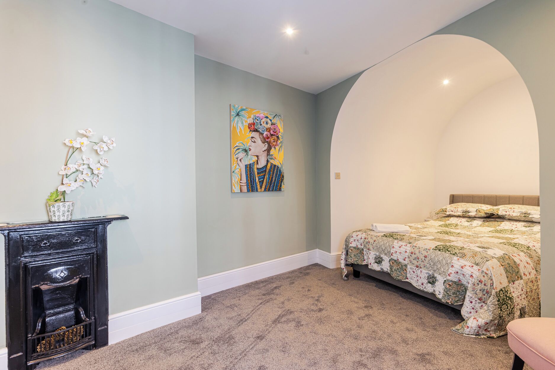 A bedroom with a bed, a nightstand, a painting, and a potted plant.