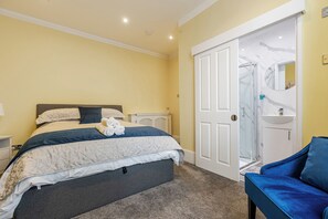 Ein Schlafzimmer mit einem Bett, einem Nachttisch, einem Stuhl, einem Badezimmer mit Waschbecken und Spiegel sowie einer Tür.