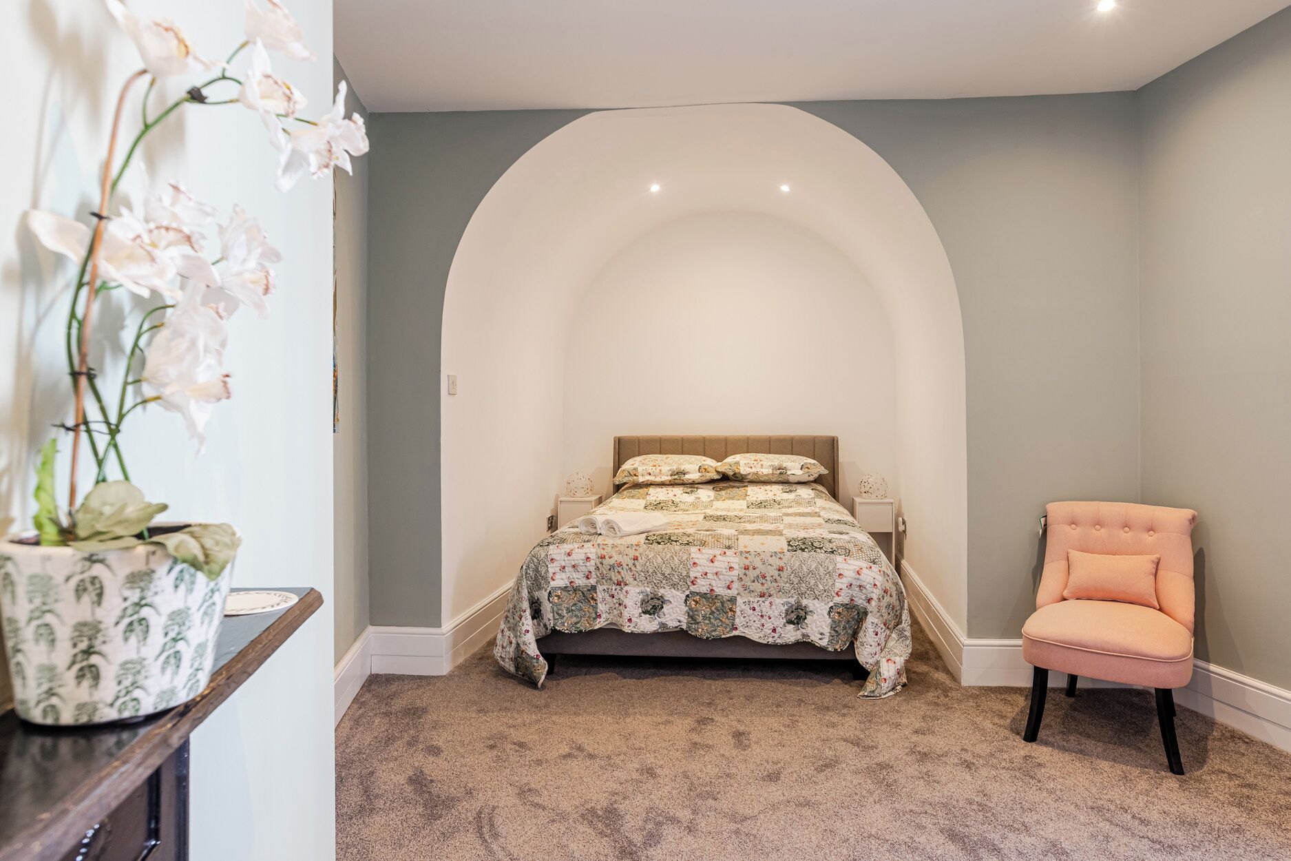 Ein Schlafzimmer mit einem Bett, einem Sessel und einer Vase mit Blumen.