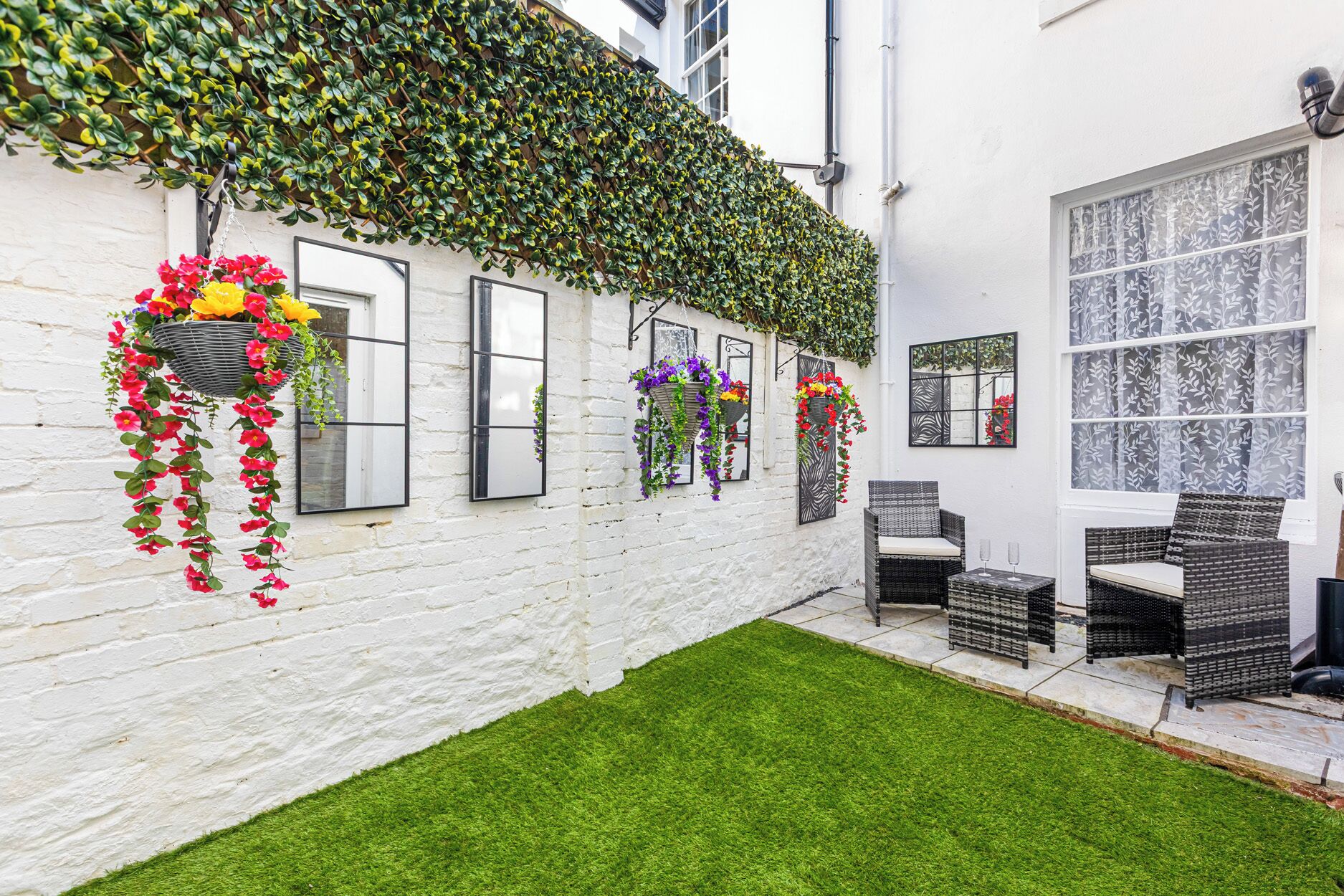 A white building with a green ivy-covered wall, outdoor seating, and a small grassy area.