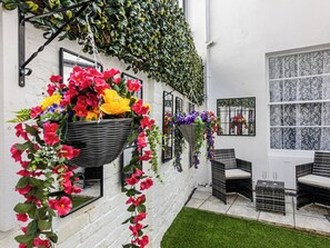 Un edificio bianco con cesti di fiori pensili, mobili da giardino in vimini e una piccola area verde.
