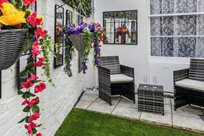 Eine Terrasse mit Korbmöbeln, einer weißen Ziegelwand und hängenden Blumenkörben.
