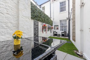 Ein weißes Gebäude mit einem Glastisch, einem Hecken und einer Terrasse mit Gartenmöbeln.