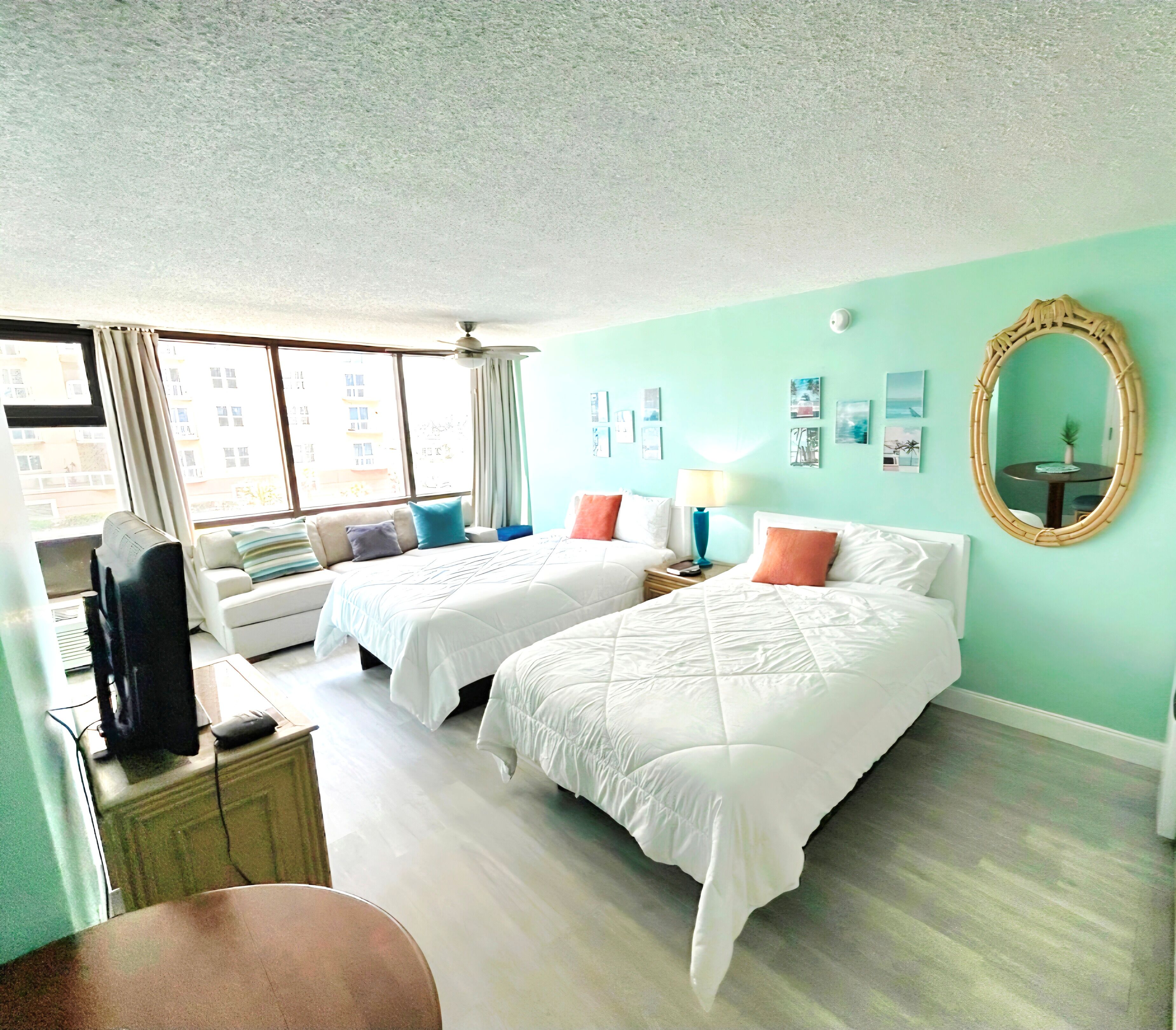 Une chambre d’hôtel avec deux lits, un bureau avec un ordinateur, une chaise, une table ronde avec une lampe et un grand miroir.