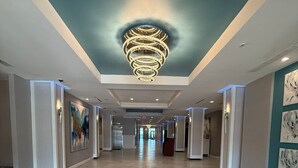 Ein geräumiger Hotelkorridor mit einem modernen Kronleuchter, Fliesenböden und Kunstwerken an den Wänden.